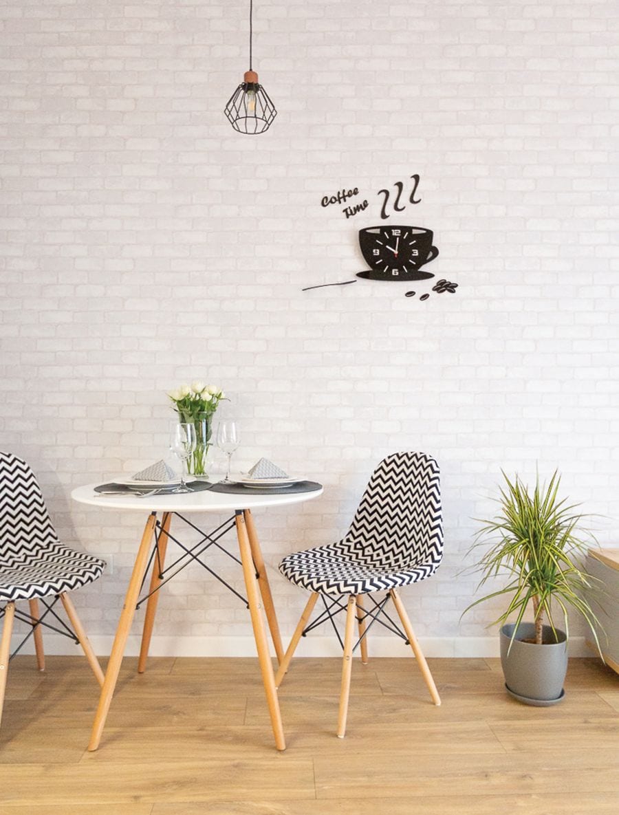 A dining area with a round table, two chairs, a potted plant, and a wall clock.