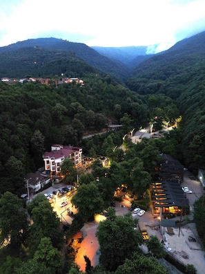A mountainous area with a building complex featuring multiple floors, a parking area, and a small bridge connecting different parts of the property. - Mersu A'la Hotel (Kartepe)