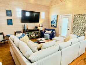 Ein Wohnzimmer mit einer großen Couch, einem Fernseher, einem Bücherregal und einer Wand mit Muster.