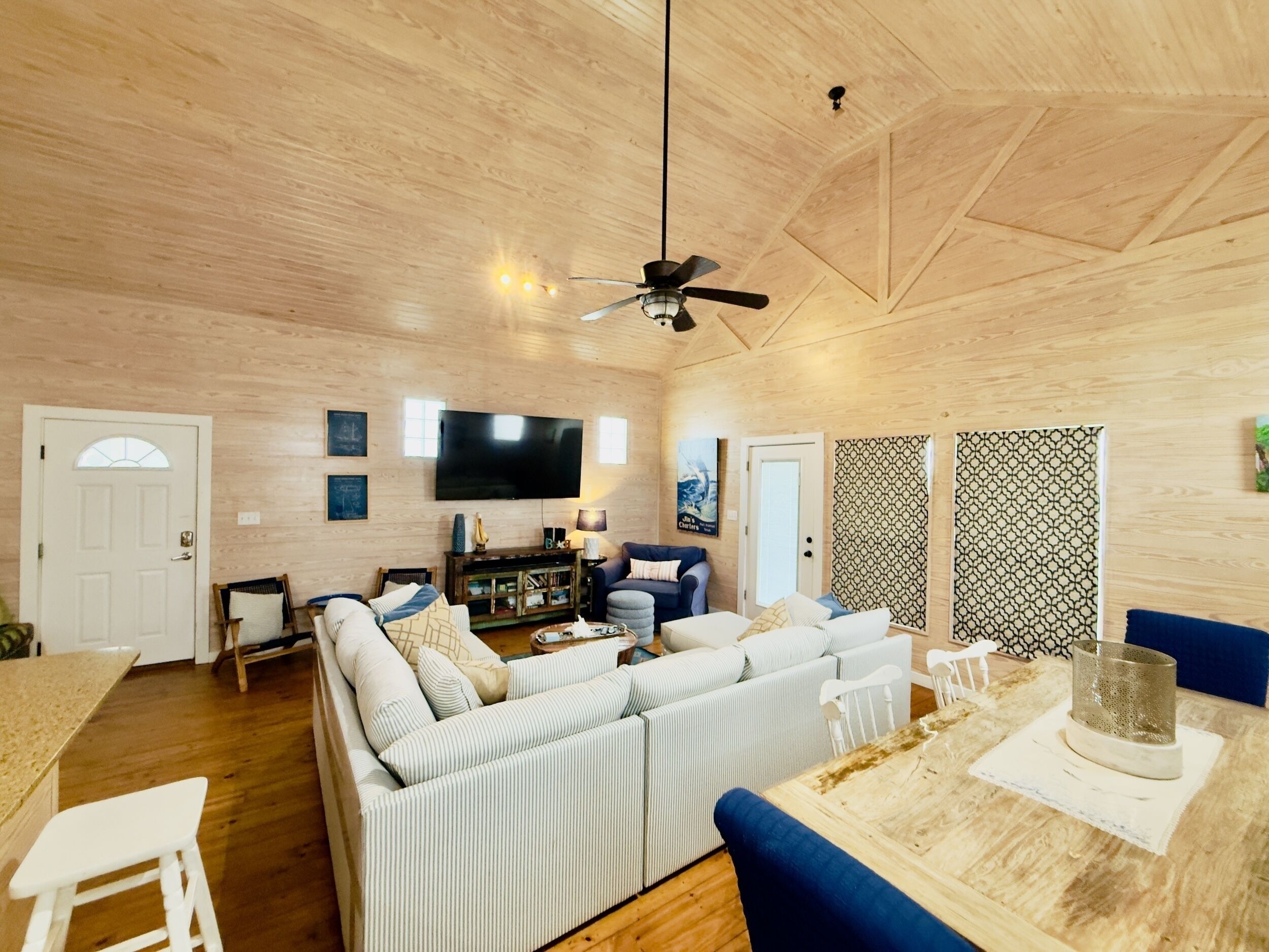 A spacious living room with a large sofa, a dining table, and a ceiling fan.