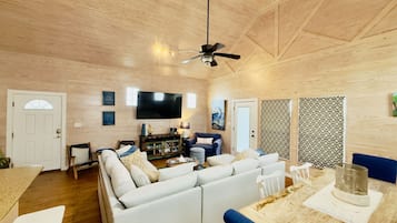 A spacious living room with a large sofa, a dining table, and a ceiling fan.