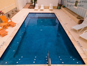 A rectangular swimming pool with a diving board, surrounded by lounge chairs and a tiled deck.