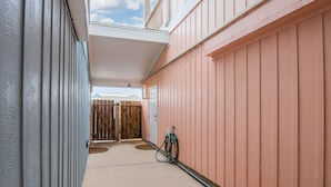 Un pasillo exterior cubierto con una puerta de madera, un carrete de manguera y una puerta.