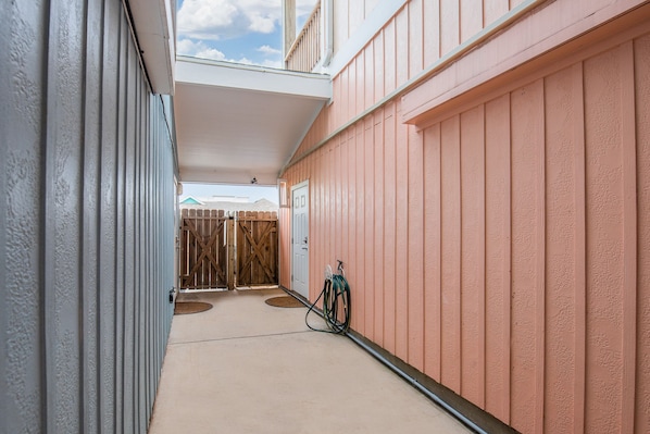 A narrow hallway with a covered area, a wooden gate, and a hose on the right.