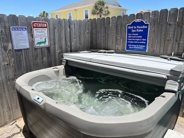 A hot tub with a wooden fence and signs indicating safety rules and spa regulations.