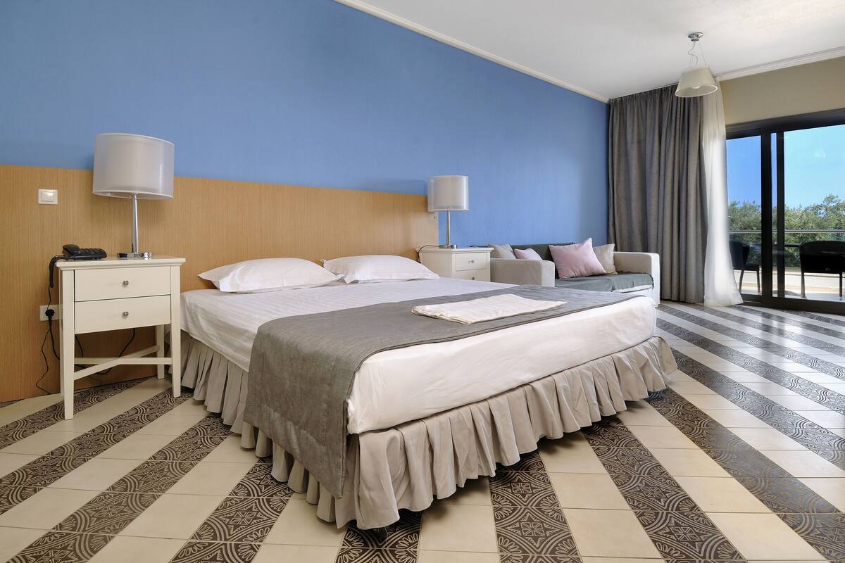 Ein Hotelzimmer mit Bett, Nachttischen, Lampe, Stuhl und Blick ins Freie.
