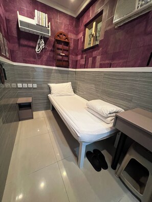 A compact hotel room with a single bed, a small bedside table, a built-in shelf with books, a wooden chair, and a small trash bin. - Hop Inn On Nathan Road (Kowloon)
