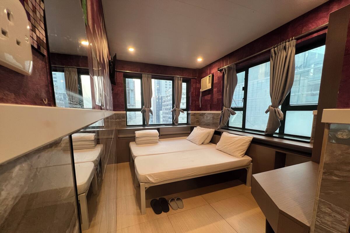 A hotel room with two beds, a window with curtains, a mirror, and a tiled floor.