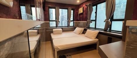 Habitación de hotel con dos camas, una ventana con cortinas, un espejo y suelo de baldosas.