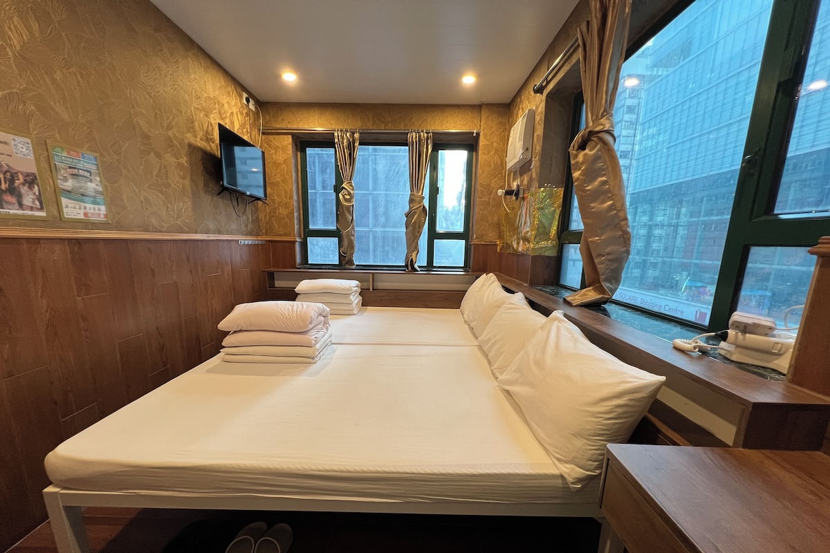 A hotel room with a large bed, a TV mounted on the wall, and a window with curtains.