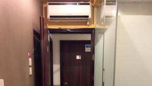 Passadís d'hotel amb una porta de fusta, un compartiment de dutxa de vidre i un aparell d'aire condicionat muntat sobre la porta.
