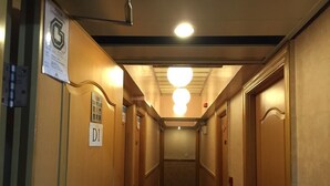 Un passadís estret amb portes de fusta, un senyal que indica la habitació D1 i una làmpada al sostre.