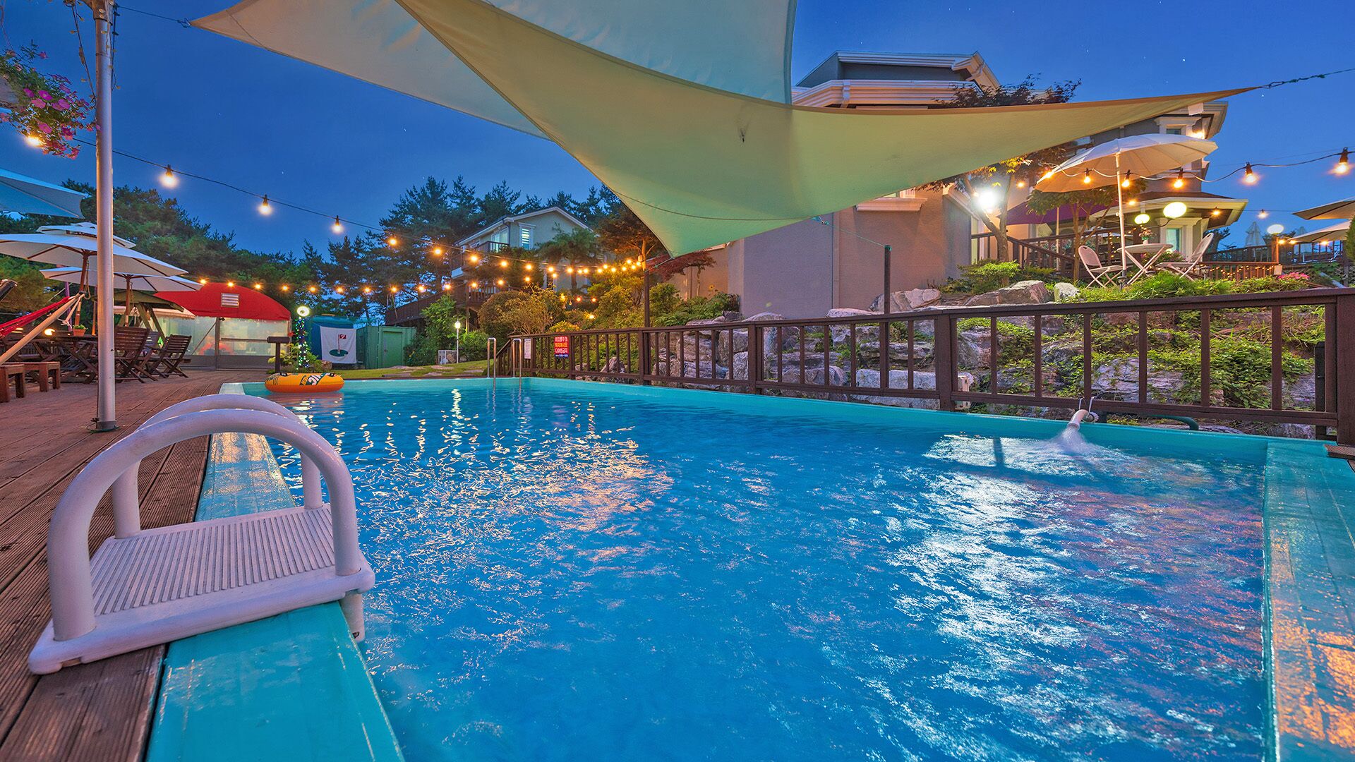 A swimming pool with a deck, surrounded by outdoor seating and string lights.