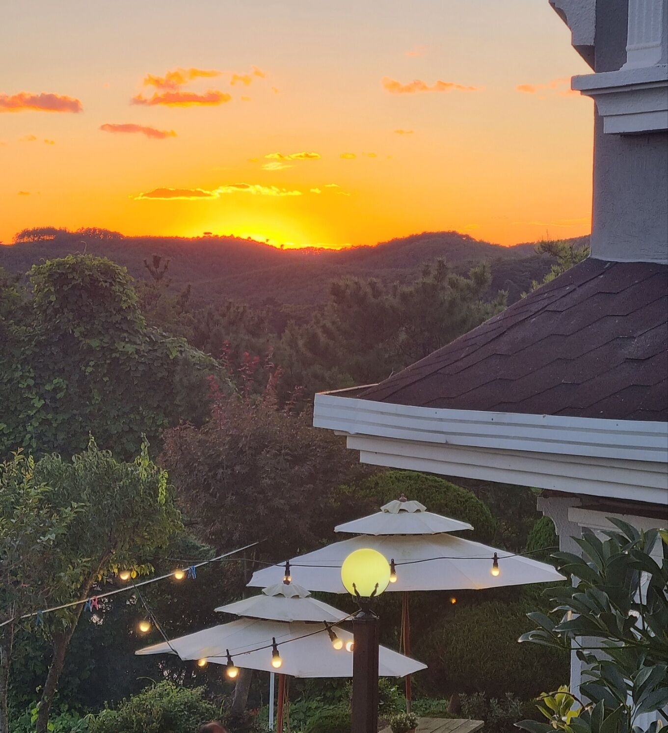 A sunset view from a balcony with string lights and umbrellas.