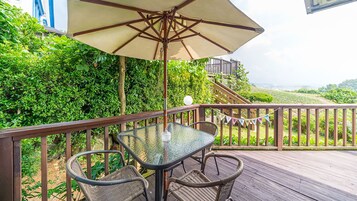 A glass table with wicker chairs and a beige umbrella on a wooden deck.