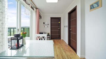 Un pasillo con una mesa de vidrio, una silla blanca, una mesita con un florero y una puerta con picaporte, además de un cuadro en la pared.