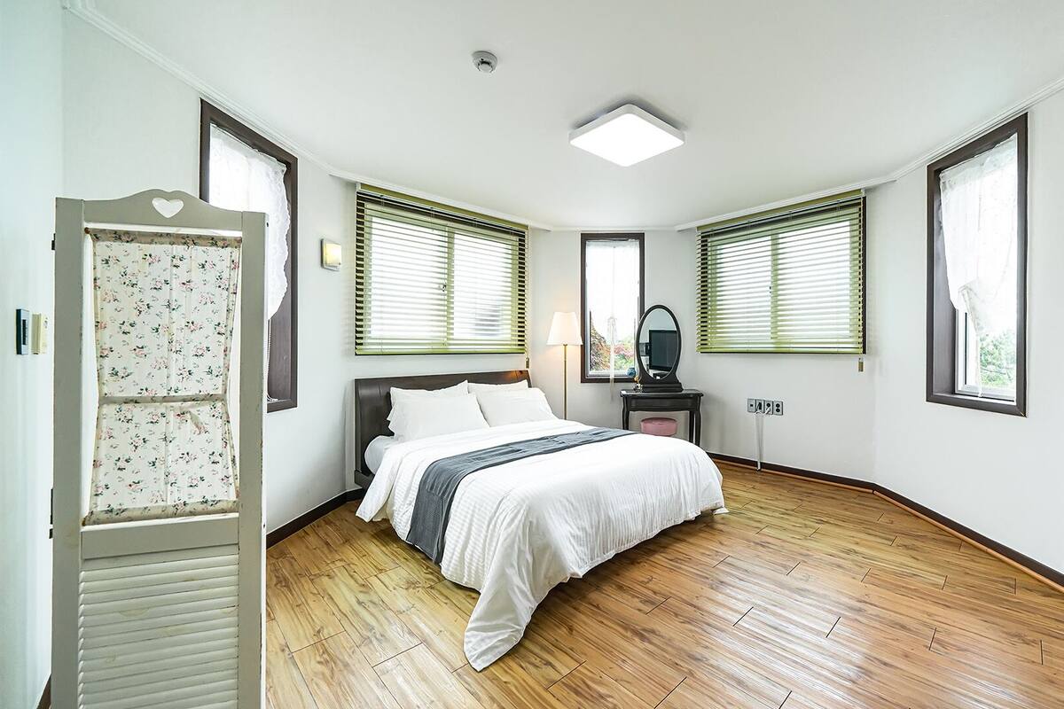 Ein Schlafzimmer mit Bett, Kommode, Spiegel und einem Fenster mit Jalousien.