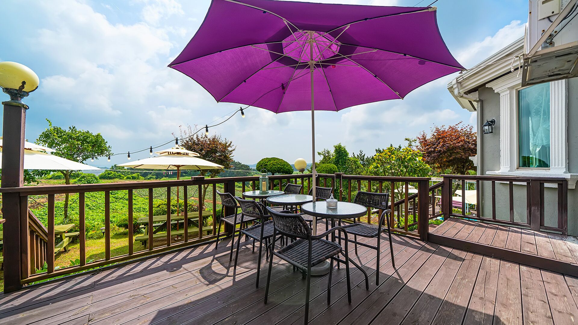 A wooden deck with outdoor furniture, including tables and chairs, and a purple umbrella providing shade.