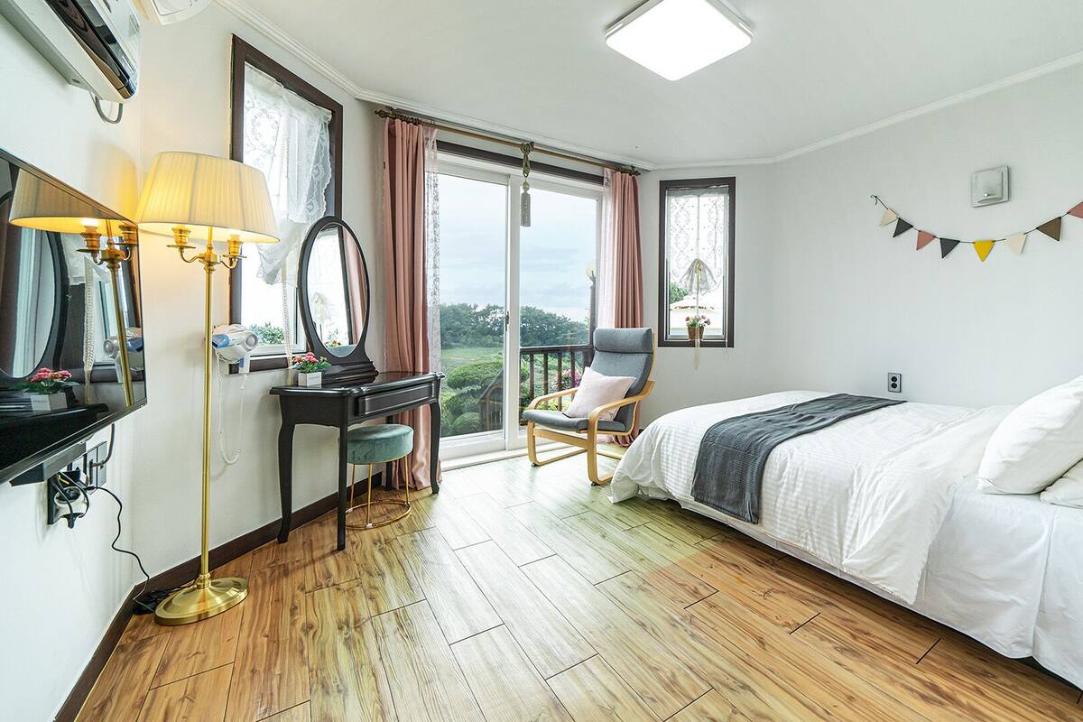 Ein Schlafzimmer mit einem Bett, einem Schreibtisch, einem Stuhl und einem großen Fenster.