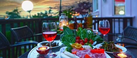 Una mesa de comedor al aire libre con platos de comida, copas de vino tinto y velas.