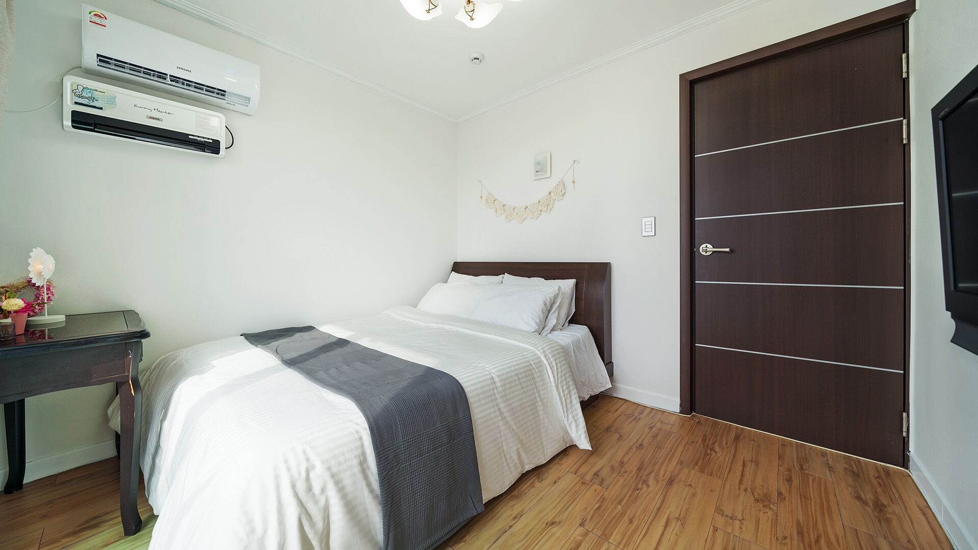 A bedroom with a bed, a desk, an air conditioner, and a wooden door.
