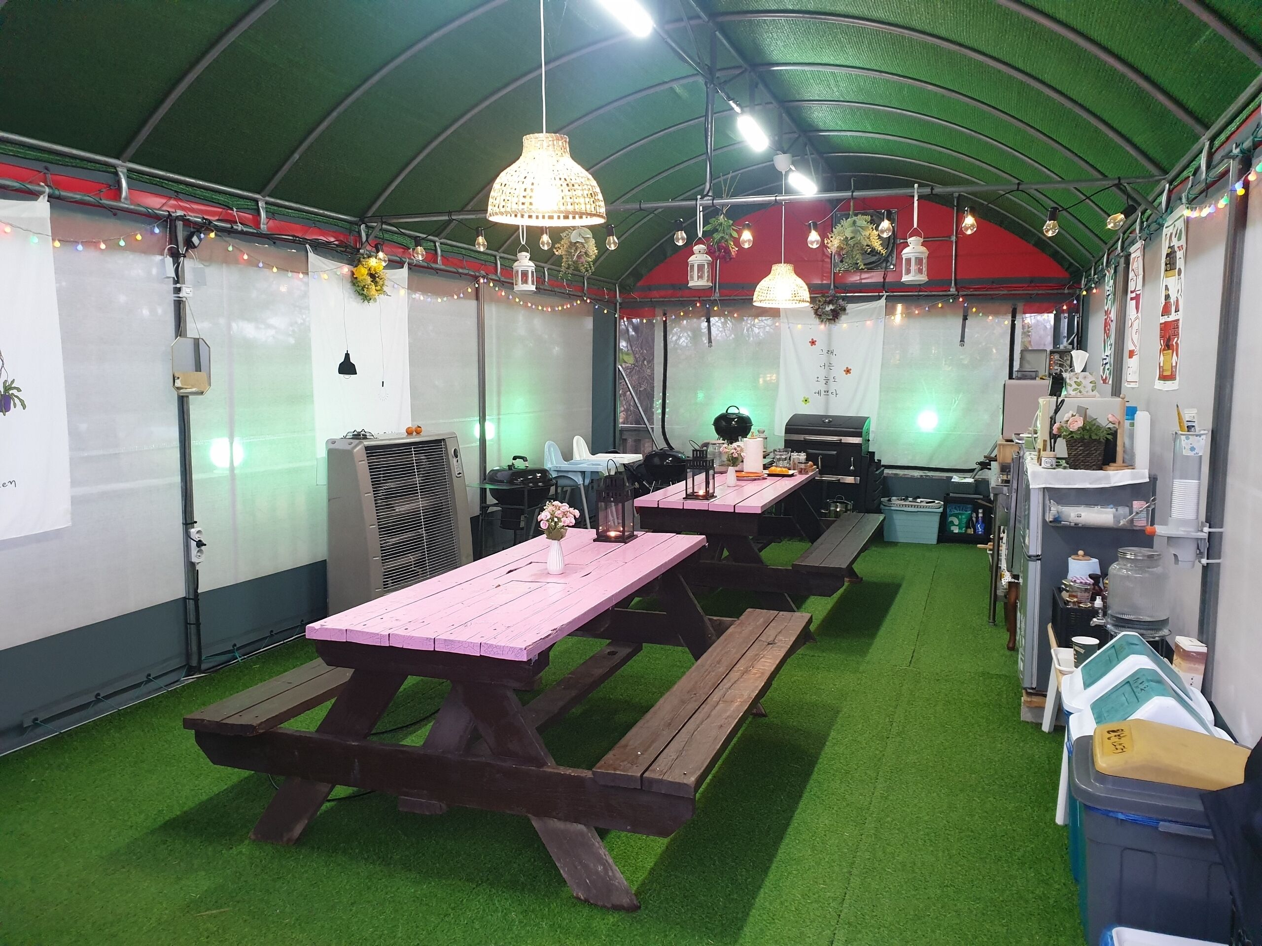 A covered outdoor area with picnic tables and benches, a grill, and various decorations.