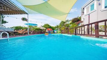 Relax by the pool surrounded by lounge chairs and umbrellas, with a water play area for kids nearby.