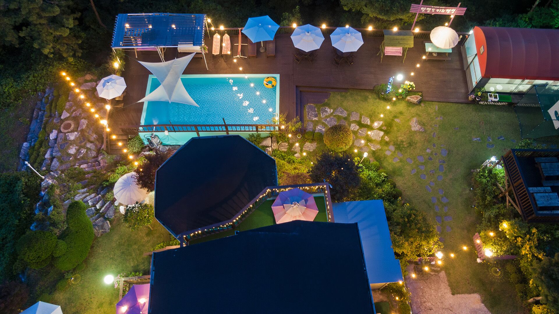 An aerial view of a backyard with a swimming pool, umbrellas, and string lights.