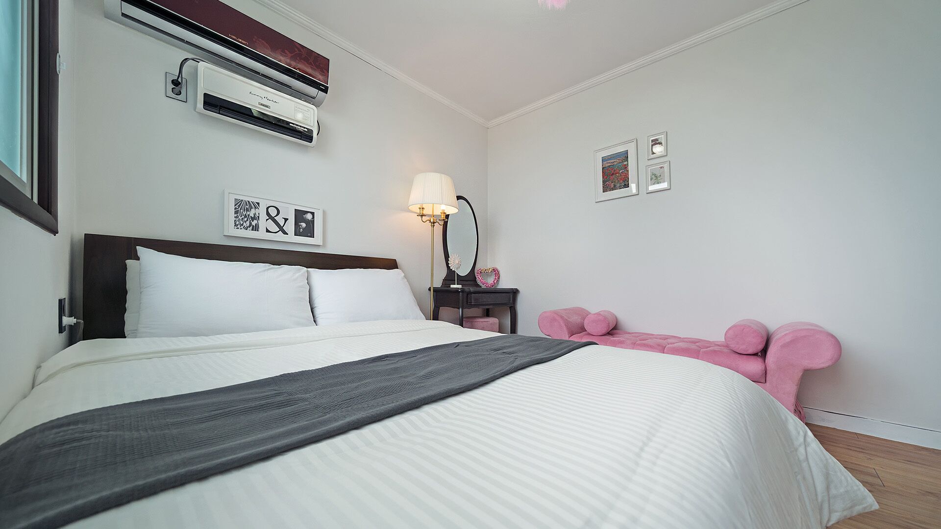 Une chambre à coucher bien rangée, avec un lit, une table de chevet, une lampe et une chaise rose.