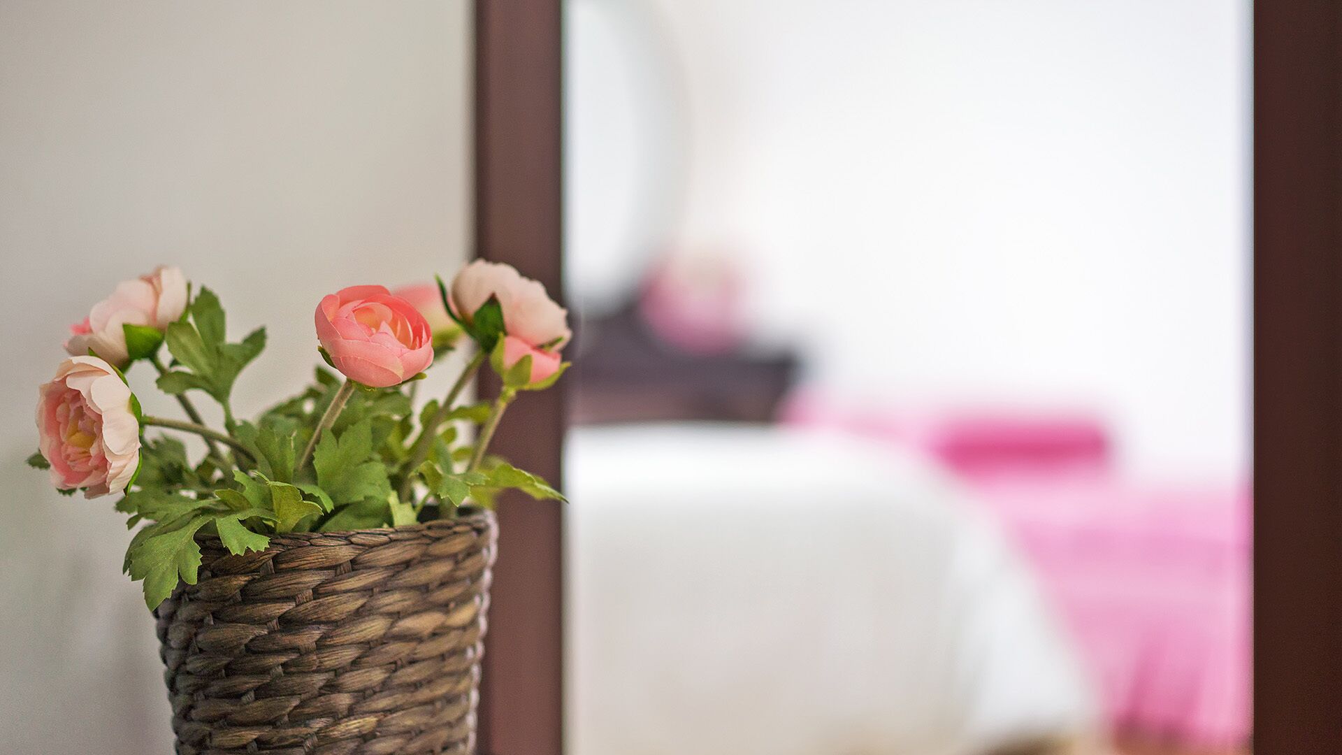 Un panier en osier orné de fleurs roses, posé sur une surface blanche.