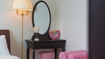 Un dormitorio con una cama, una mesita de noche con lámpara, un espejo y una silla rosa.