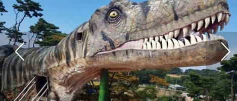 A large dinosaur statue with a visible eye and teeth, a green support structure, and a signboard.