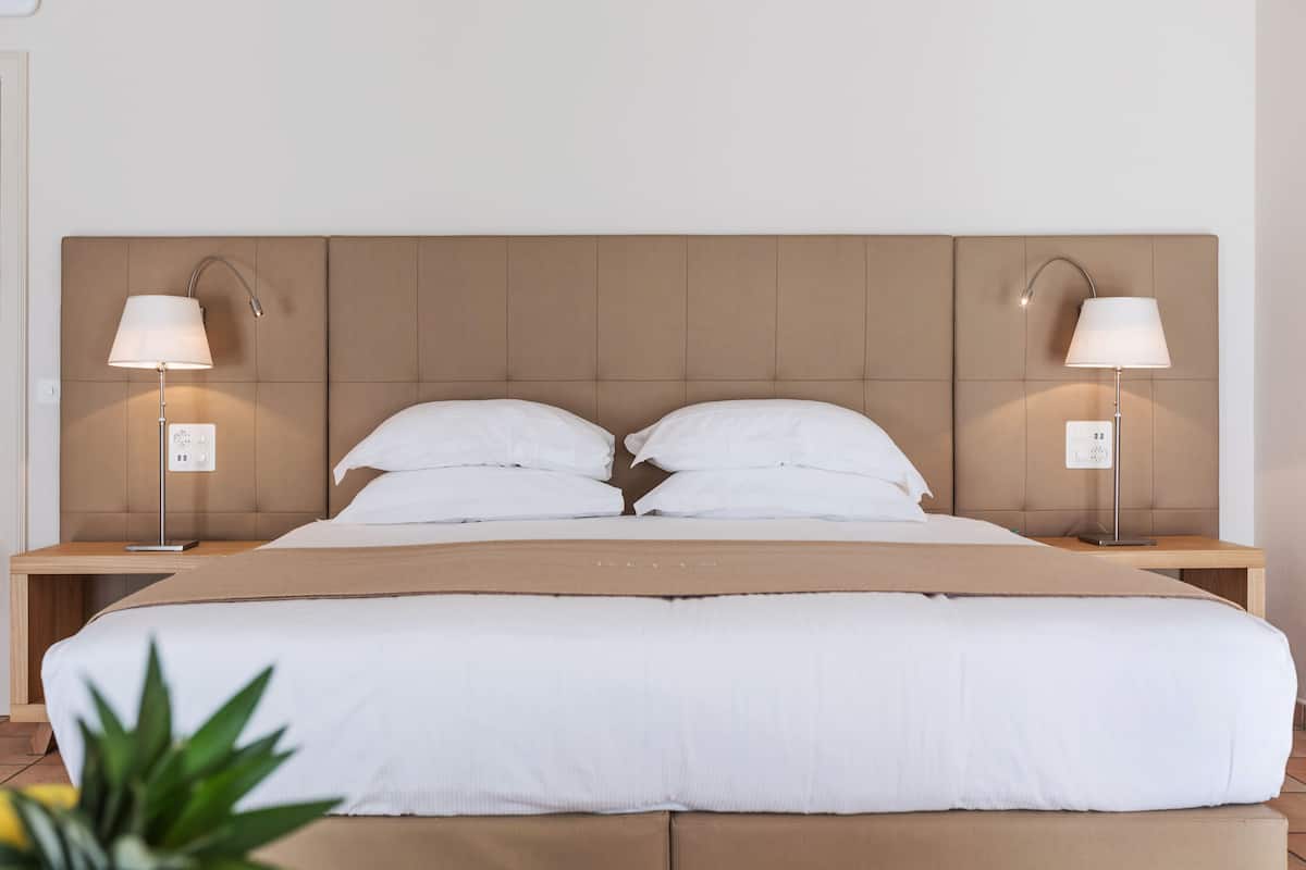 Una habitación de hotel con una cama grande, dos mesitas de noche y dos lámparas fijadas a la pared.