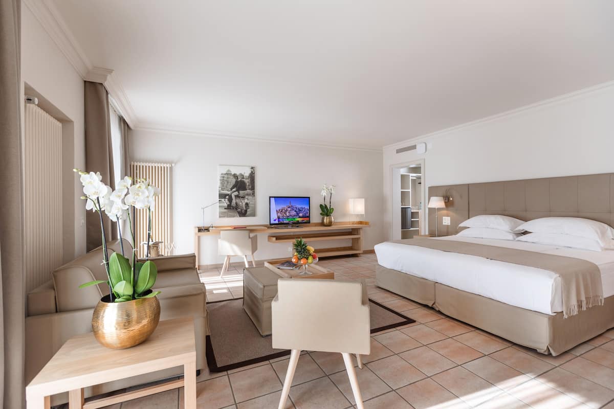 Habitación de hotel moderna con cama, escritorio, silla, televisor y planta en maceta.