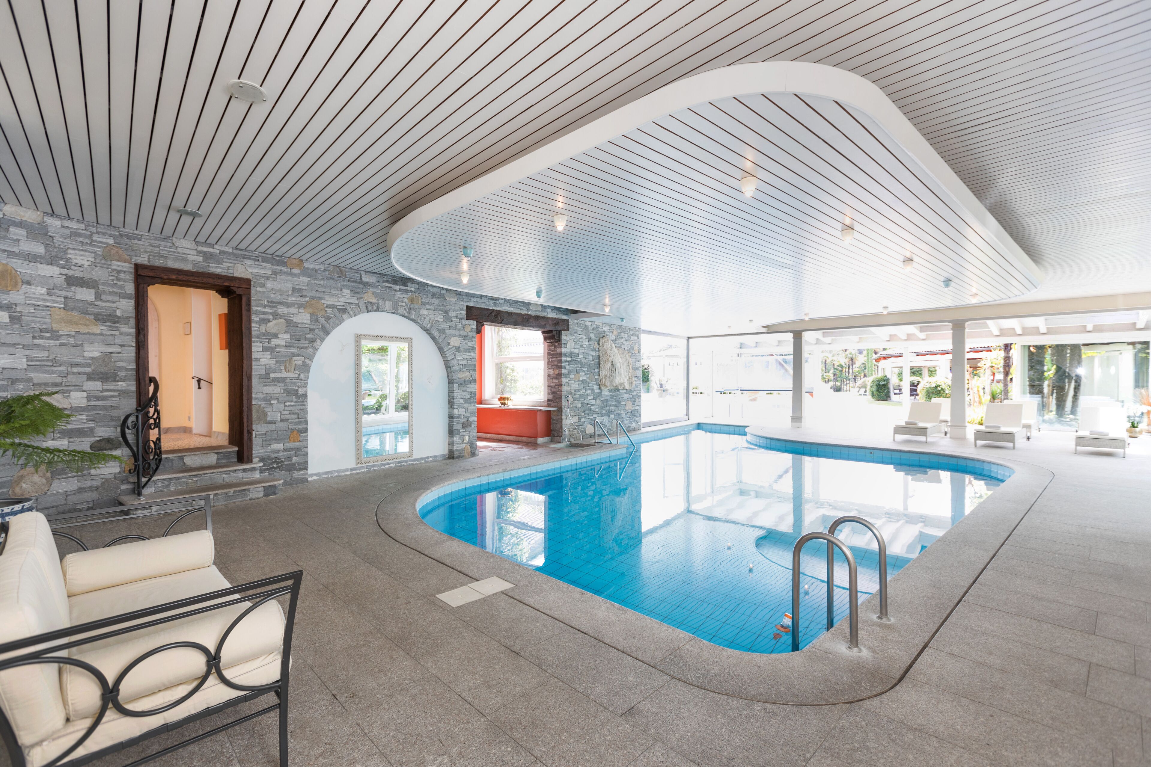 Ein innenliegender Pool mit gebogenem Design, Steinwänden und moderner Beleuchtung.