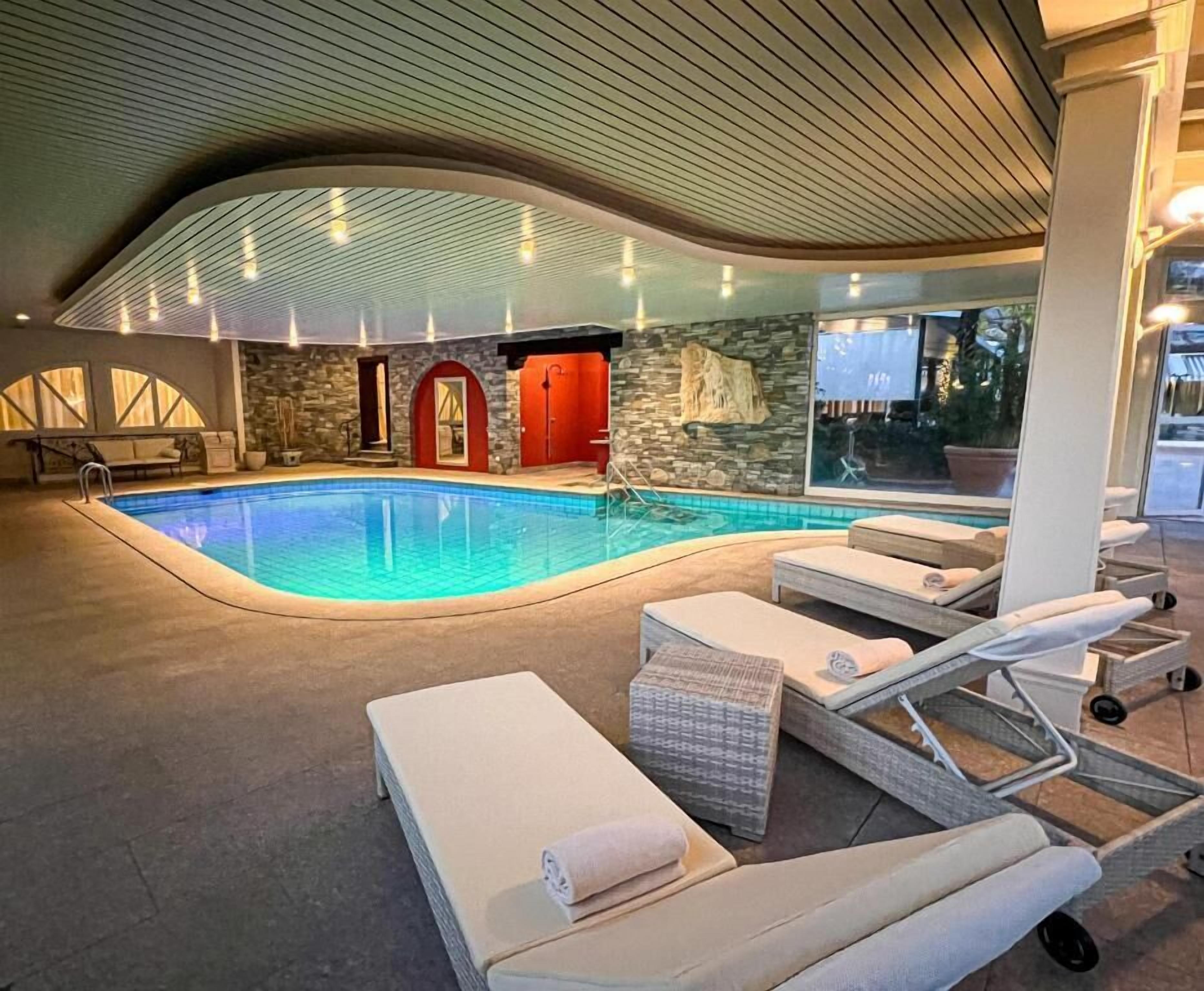 Une piscine intérieure dotée de chaises longues et d’un mur en pierre.