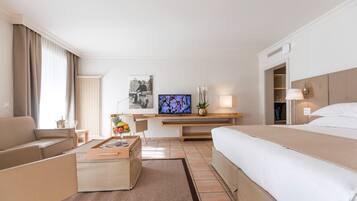 Une chambre d’hôtel comprenant un lit, un canapé, un bureau avec une télévision, une petite table avec un vase et une fenêtre avec des rideaux.