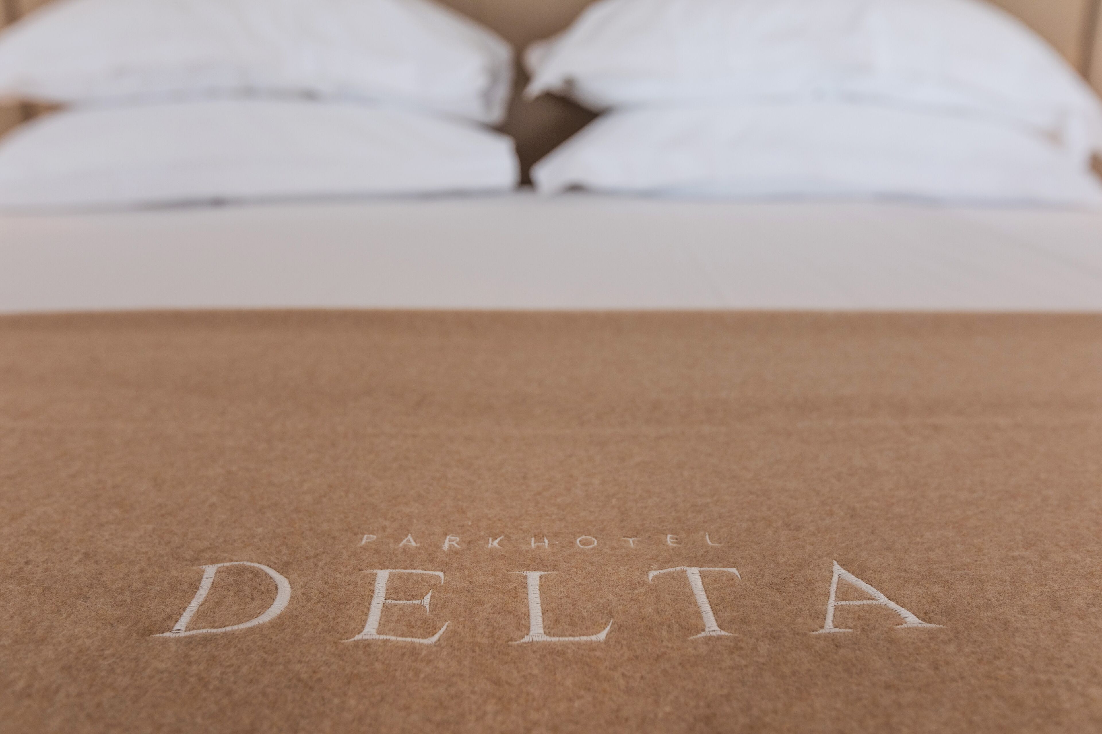 Una cama con ropa blanca y una cubierta marrón con el bordado 'PARKHOTEL DELTA'.