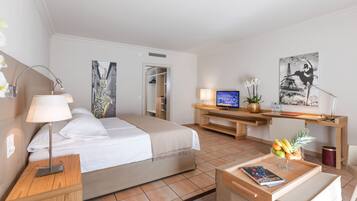 A hotel room with a bed, bedside table, lamp, TV, desk, chair, and artwork.