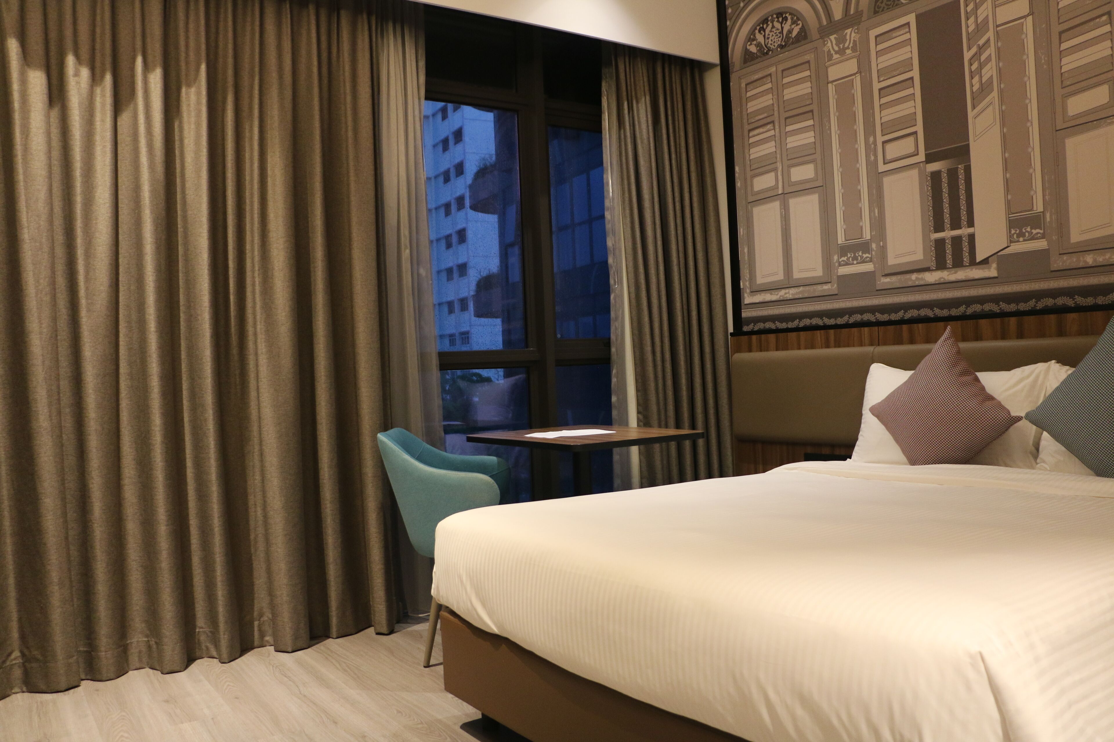 Habitación de hotel con cama, una mesita, una silla y ventana con cortinas.