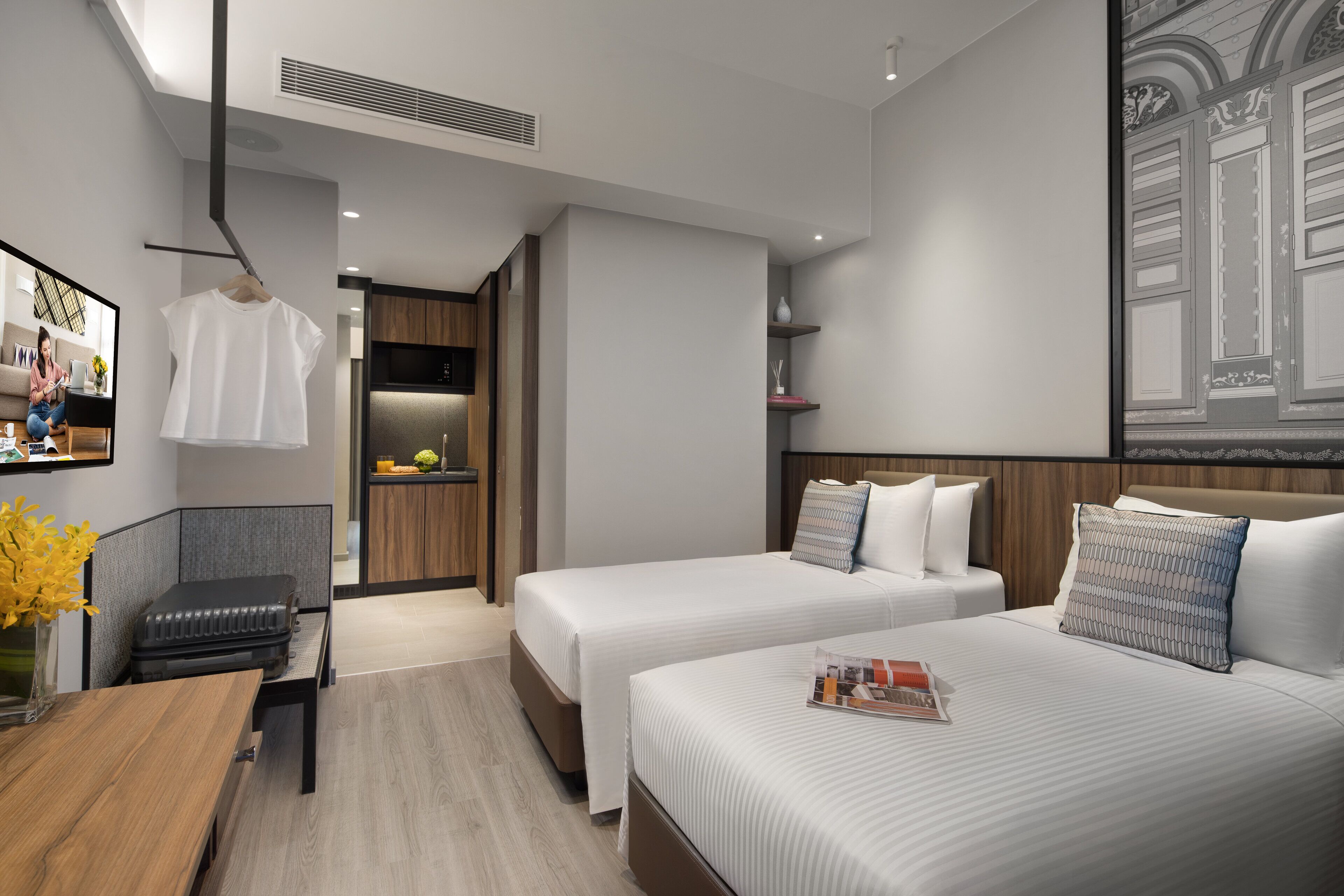 Een moderne hotelkamer met twee bedden, een houten bureau, een stoel, een klein tafeltje met een vaas en een spiegel.
