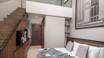 Un dormitorio moderno con una cama grande, un televisor en la pared y una escalera que sube a un nivel superior.