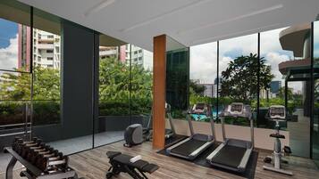 Un gimnasio moderno con cintas de correr, mancuernas y equipamiento de ejercicio, amplias ventanas y vistas a zonas verdes y edificios.