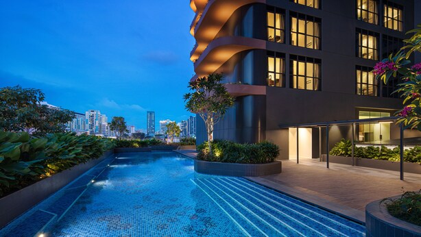 A modern building with a swimming pool, surrounded by greenery and illuminated windows. - Citadines Rochor Singapore (Singapore)