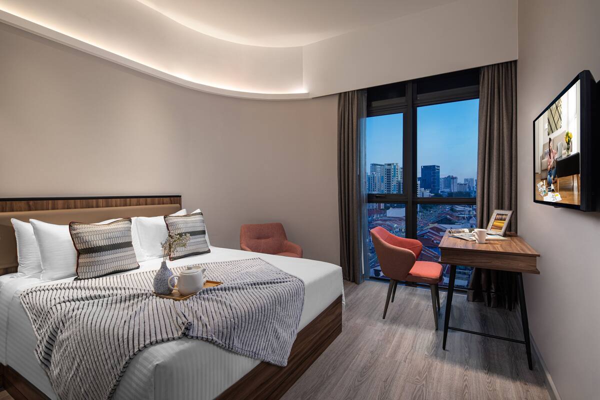 A modern hotel room with a large bed, a desk, and a city view.