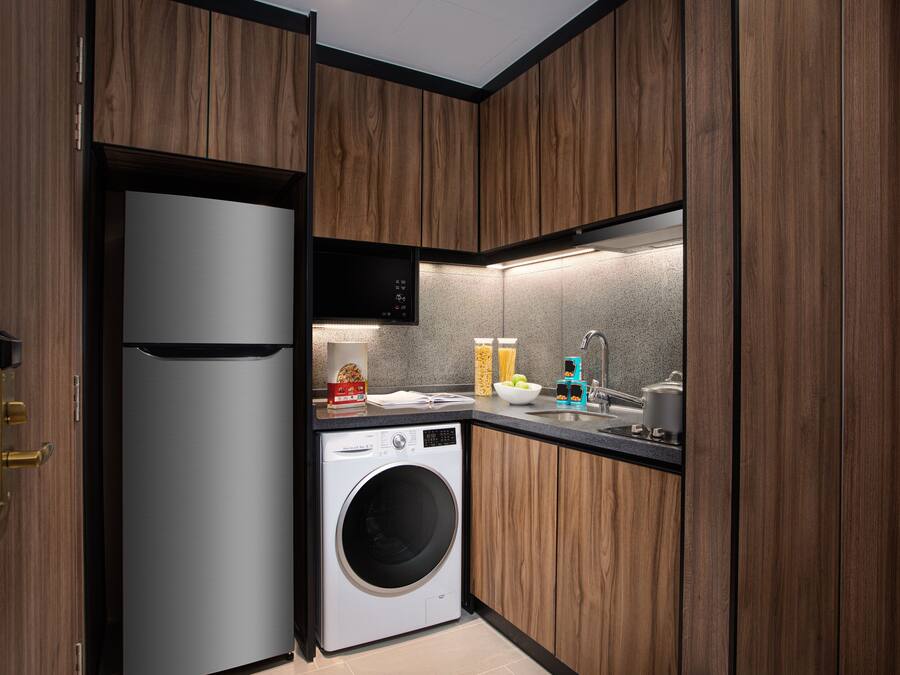 A compact kitchen with wooden cabinets, a built-in washing machine, a microwave, and a sink.