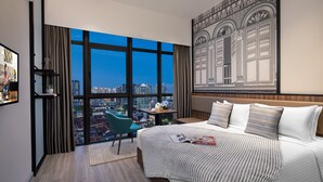 A hotel room with a large bed, a view of the cityscape, a desk with a lamp, and a chair. - Citadines Rochor Singapore (Singapore)