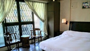 A hotel room with a large bed, two wooden chairs, a small table, and a window with curtains. - Coffee Street Homestay (Gukeng)
