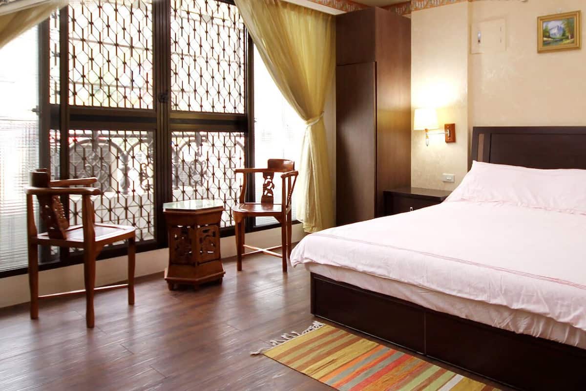 A hotel room with a large bed, wooden furniture, and a view through a window with a curtain.