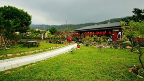 A traditional building with a red exterior, surrounded by a well-maintained garden with pathways and seating areas. - Coffee Street Homestay (Gukeng)
